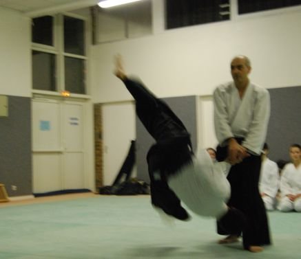 Photo en mouvement : un partenaire, jambes en l’air, chute à côté d’un pratiquant resté debout.